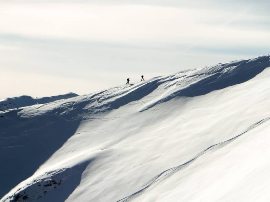 backcountry-skiers-off-in-distance-climbing-along-snow-covered-ridge