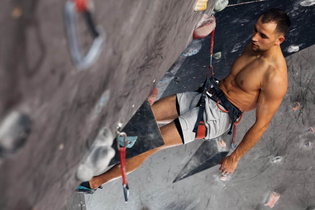 shirtless-man-resting-mid-climb-on-indoor-climbing-wall