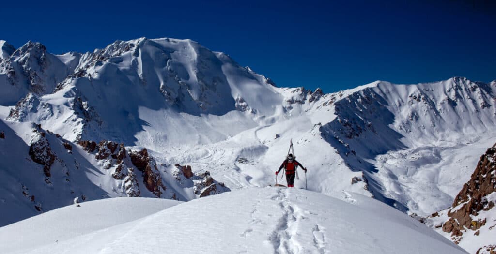 backcountry-skier-cresting-summit-white-snowy-mountains-in-background