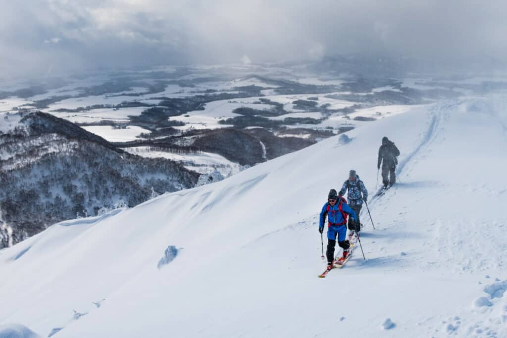 three-backcountry-skiers-touring-up-ridge-long-way-from-home-valley-down-below