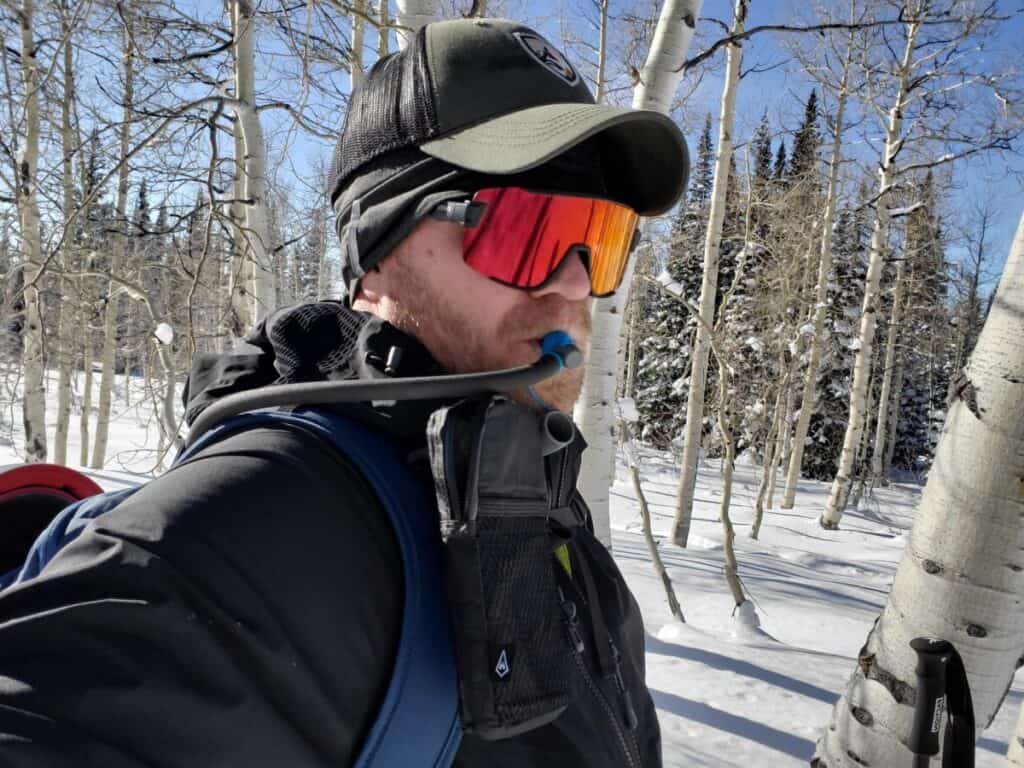 bearded-man-with-sunglasses-drinking-from-hydration-tube-in-snow-covered-aspens