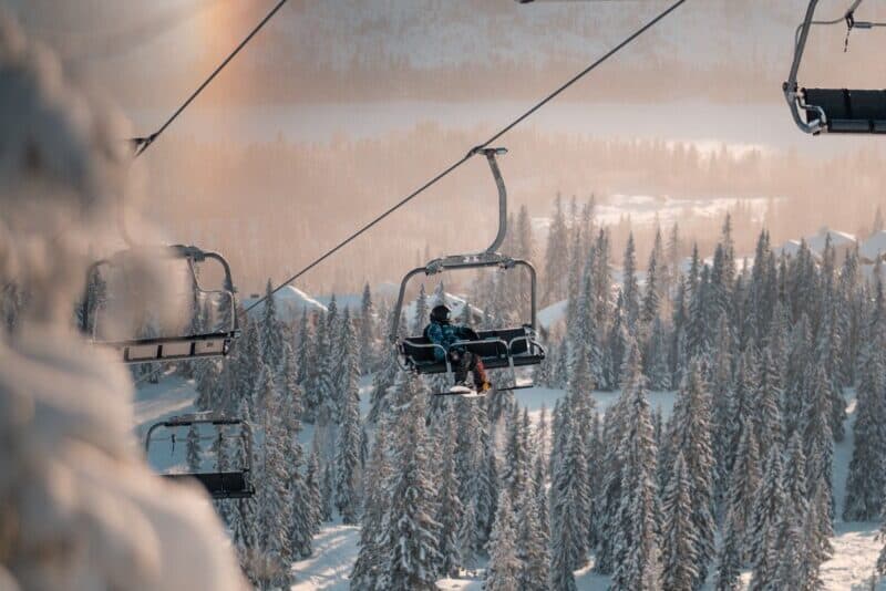 lone-snowboarder-bundled-up-and-riding-ski-lift-amidst-snow-covered-evergreens